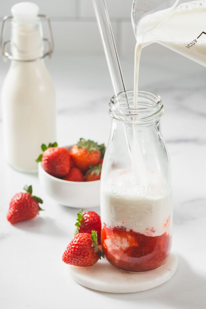 Pouring milk into a bottle of strawberry jam to make homemade korean strawberry milk.