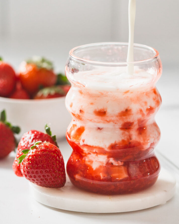 Someone pouring milk into a glass of homemade korean strawberry milk.