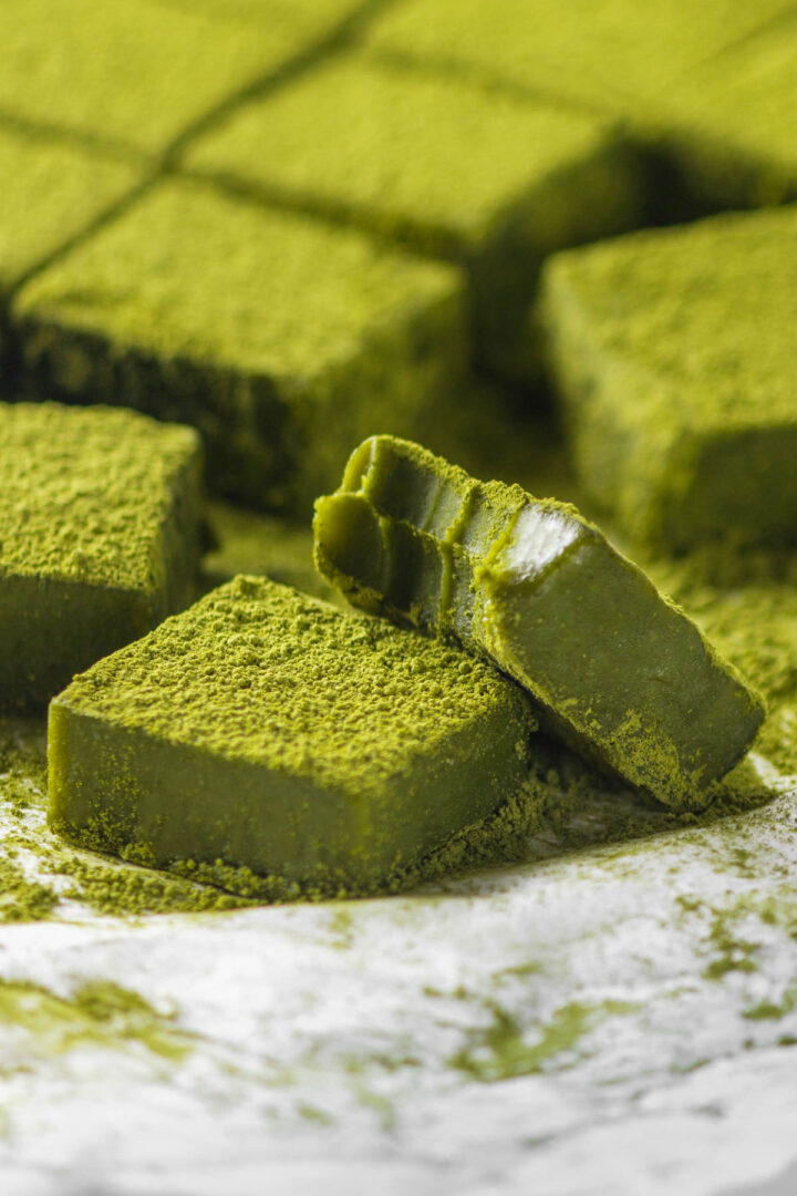 Close-up shot of a bitten square of Matcha Nama Chocolate leaning against another Nama Matcha Chocolate.