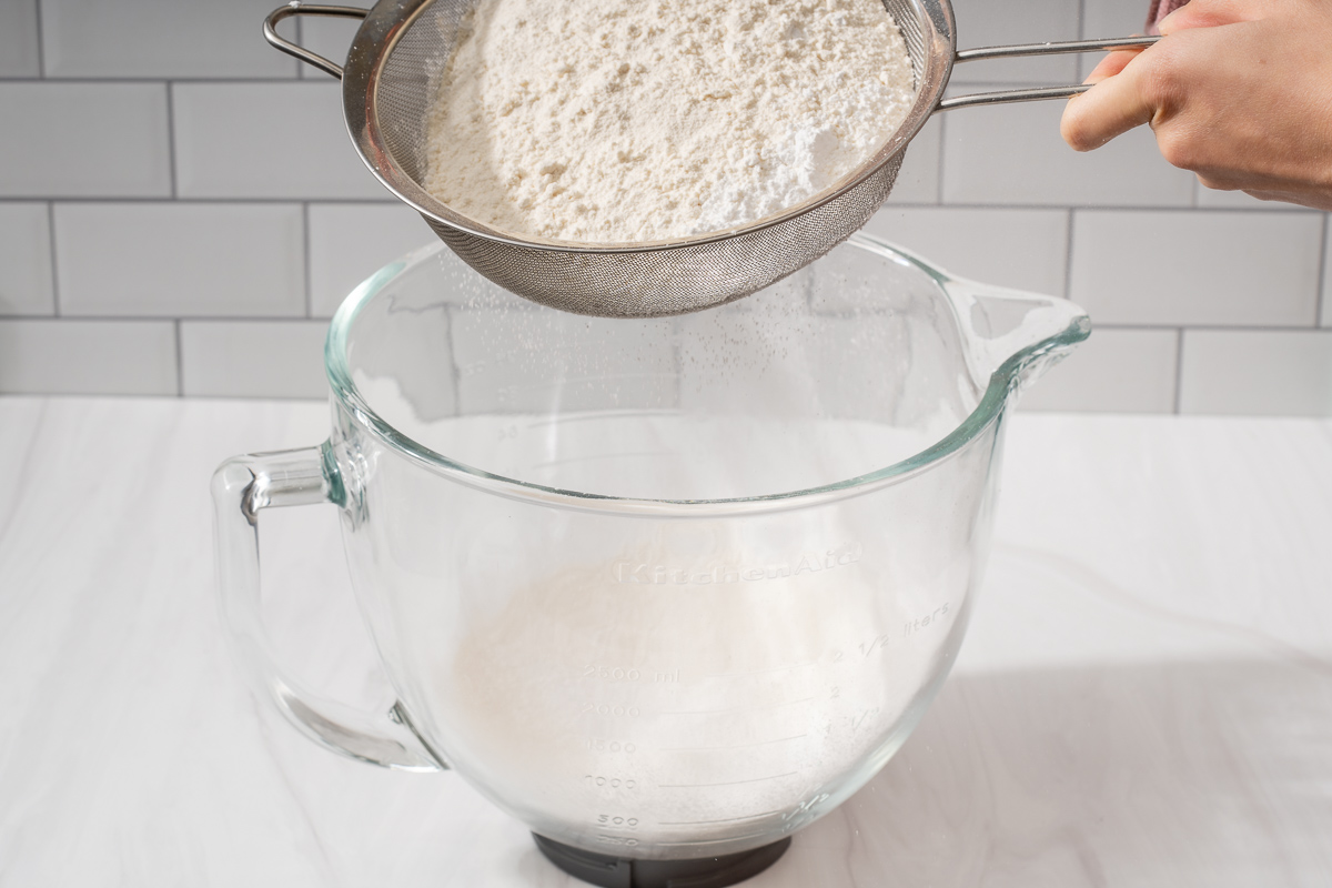 Sifting dry ingredients into a larger stand mixer bowl.