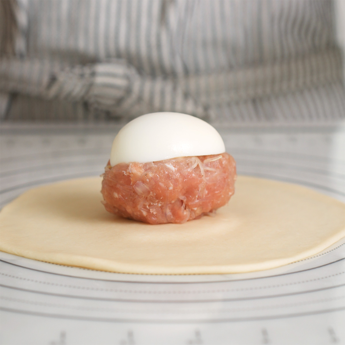 A meatball and egg sitting on a rolled out disc of dough.