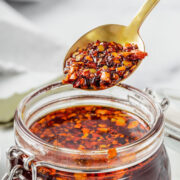 A spoon holding chili oil above a jar.