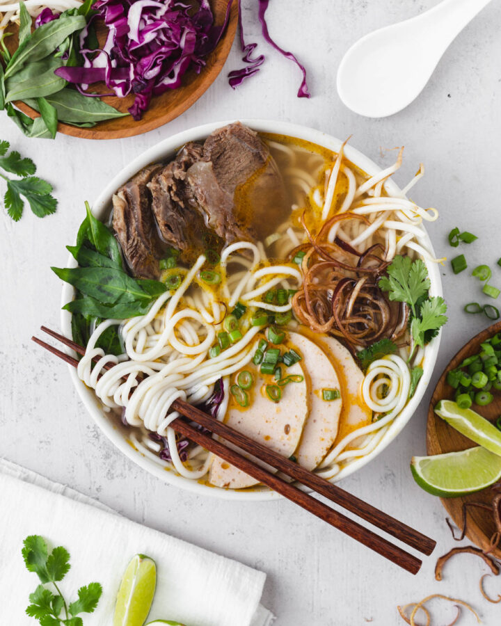 Bun bo hue bowl with ingredients sprinkled around it