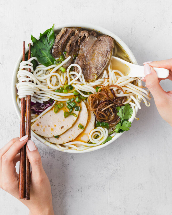 Eating beef noodle soup with chopsticks and spoon.