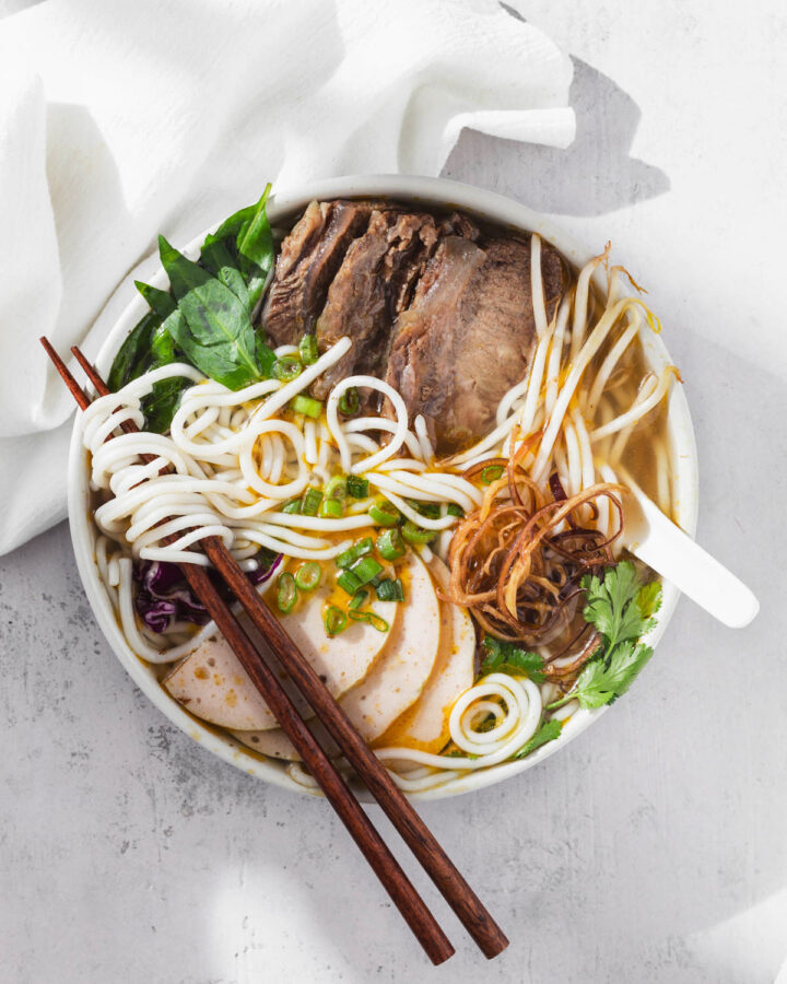 Stylized bun bo hue with toppings and chopsticks and spoon.