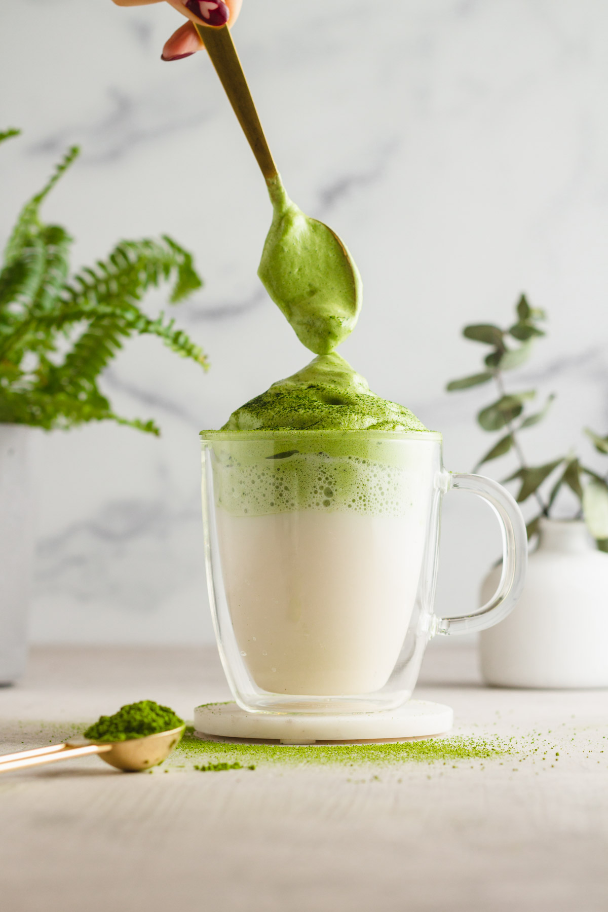 A spoon placing the foam ontop of a matcha dalgona.