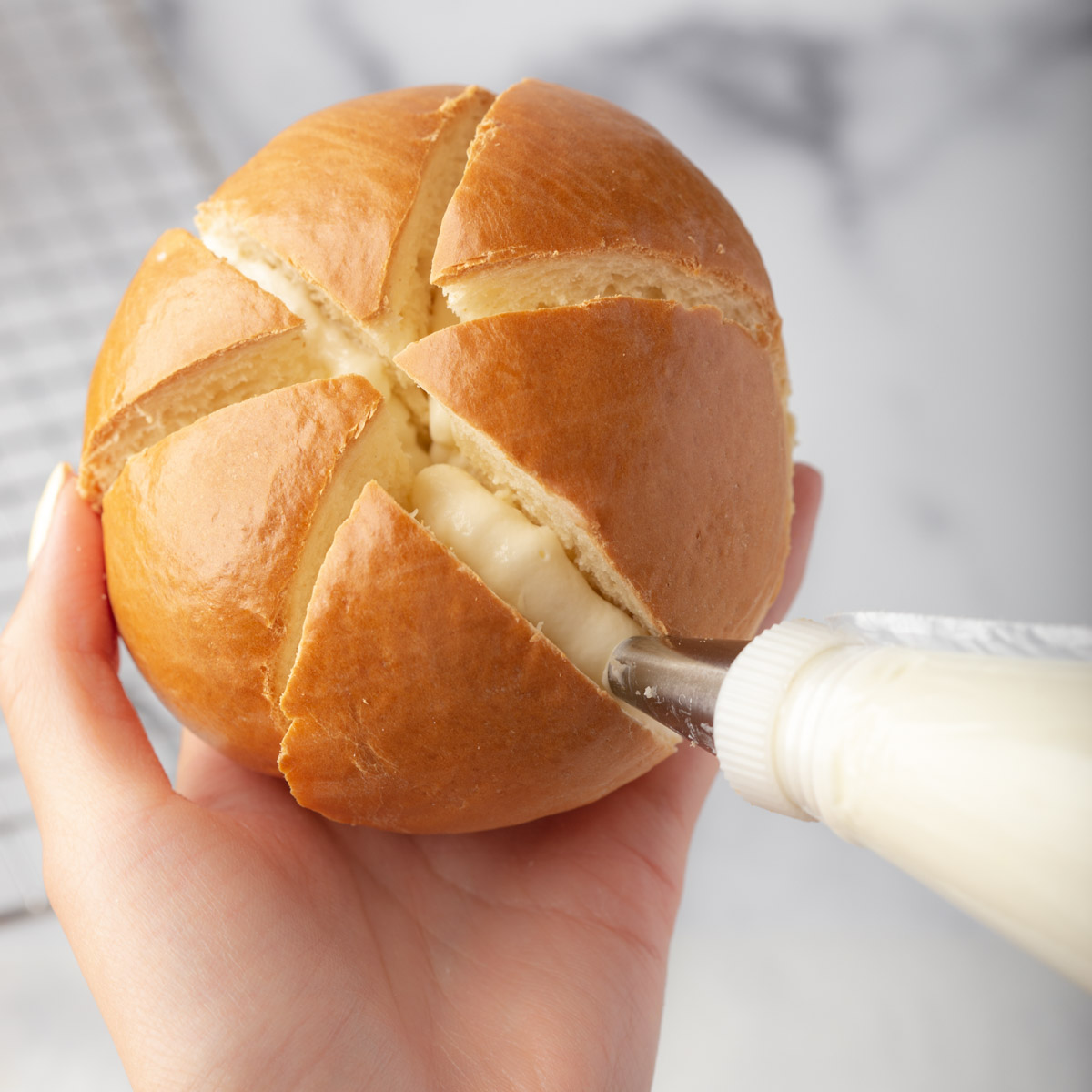 piping cream cheese into a sliced bun