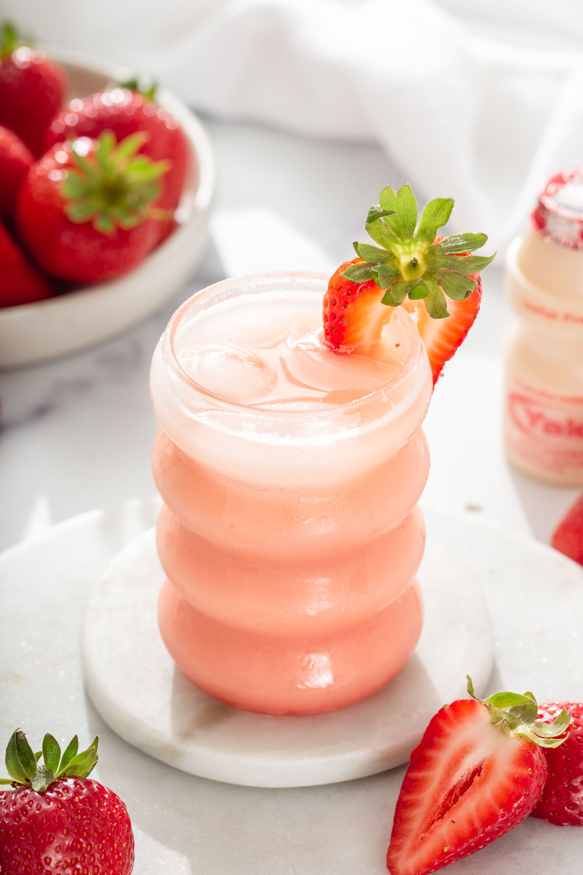 Glass of strawberry yakult tea refresher surrounded by strawberries