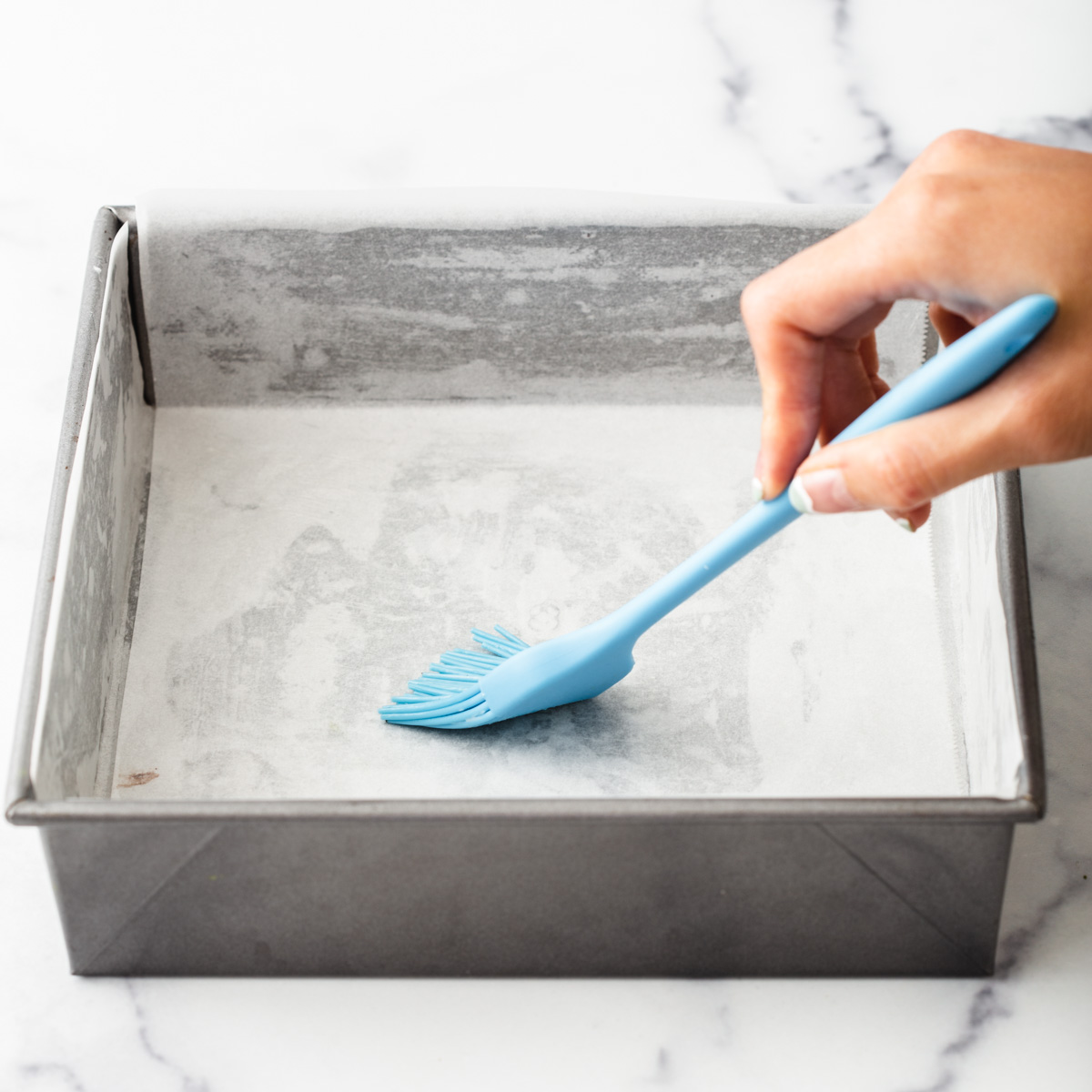 someone brushing oil onto a baking pan