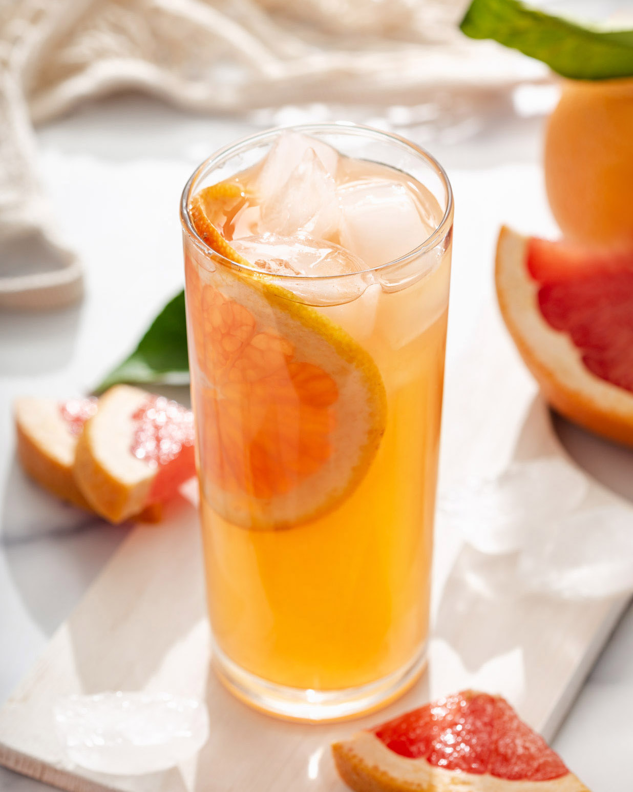 A glass of grapefruit infused green tea on a table with fresh sliced grapefruit around it.