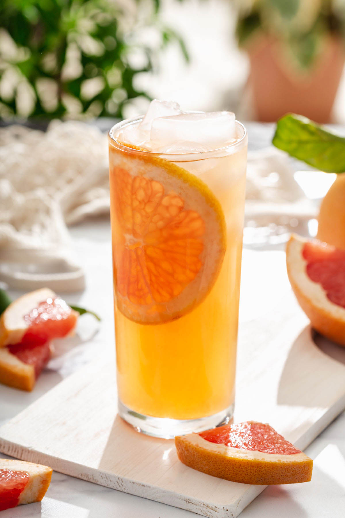 A glass of grapefruit infused green tea on a table outside surrounded by flesh cut grapefruit and plants.