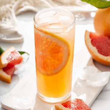 Close up of glass of grapefruit infused green tea on a table with fresh sliced grapefruit around it.