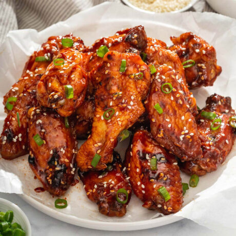 Close up of a plate of grilled Korean chicken wings smothered in sauce, scallions, and sesame seeds.