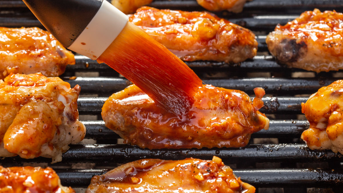 Close up of someone basting chicken wings