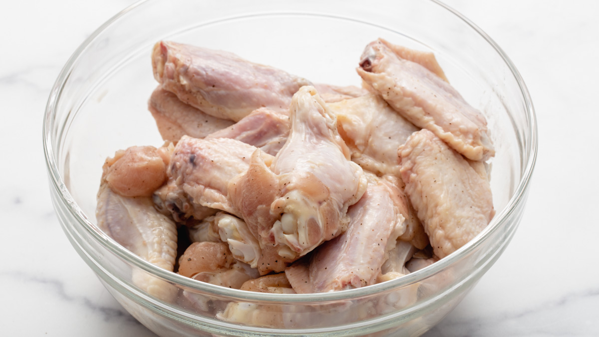 A bowl of raw chicken wings in a bowl coated with salt and pepper
