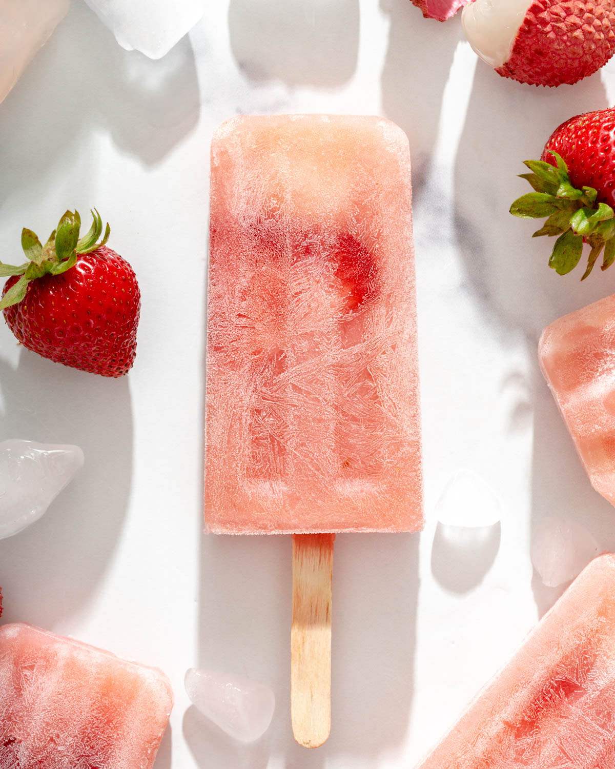 Close up of a lychee frose popsicle on a table with popsicles and fruit around it.