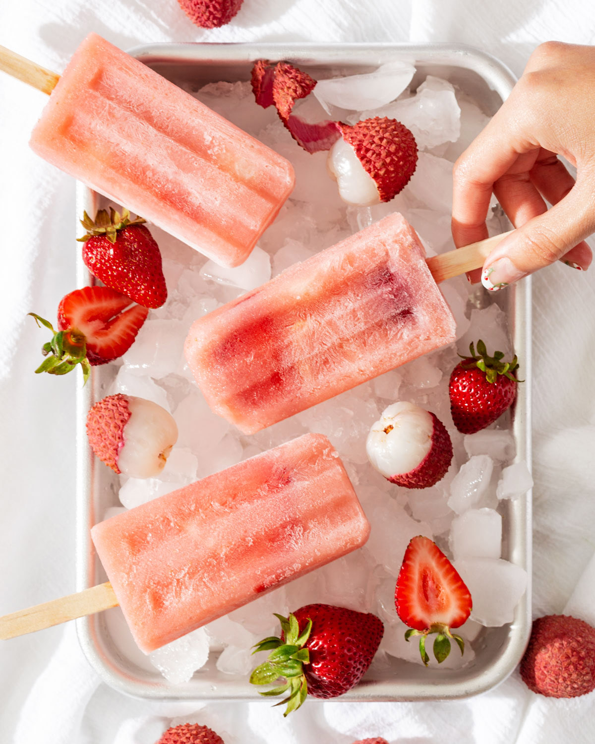 Someone grabbing a popsicle from a tray of ice, fruit, and popsicles.