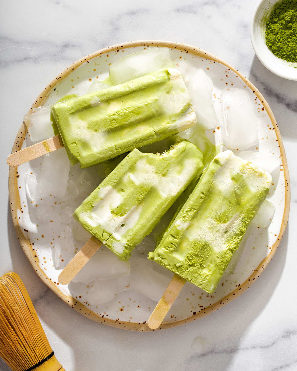A plate of matcha popsicles with a bite out of one of them.