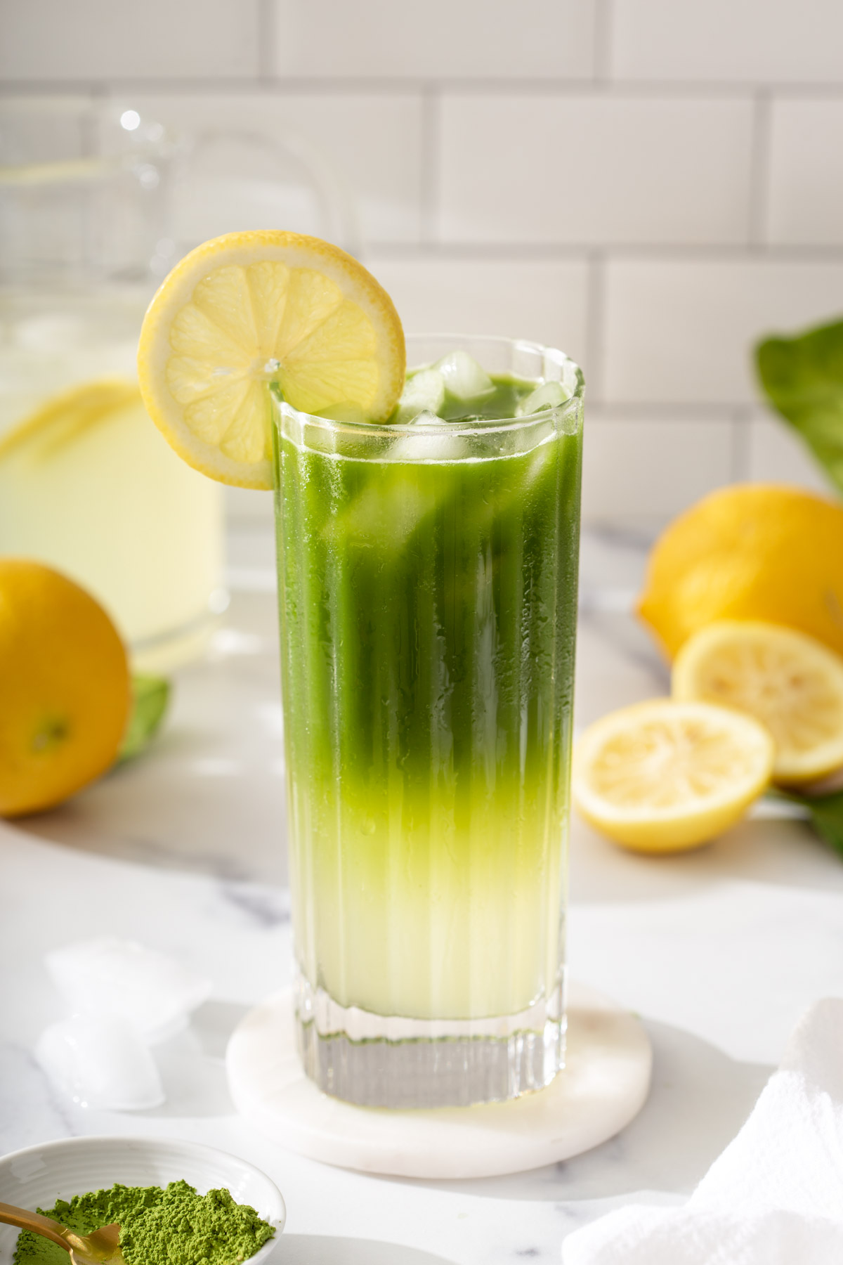 A glass of Matcha lemonade with lemons around it