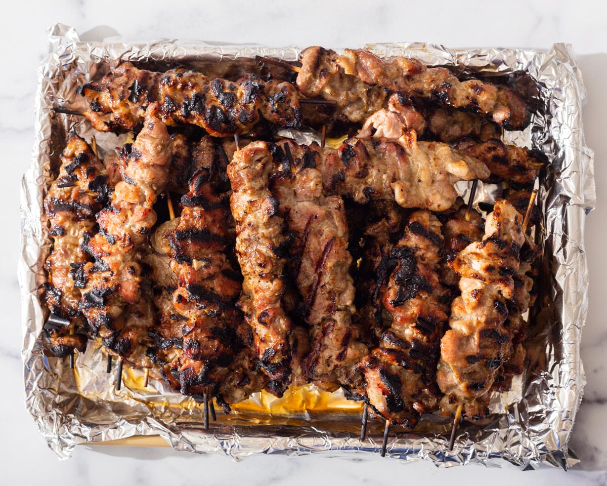 Grilled pork skewers in an aluminum foil lined tray.