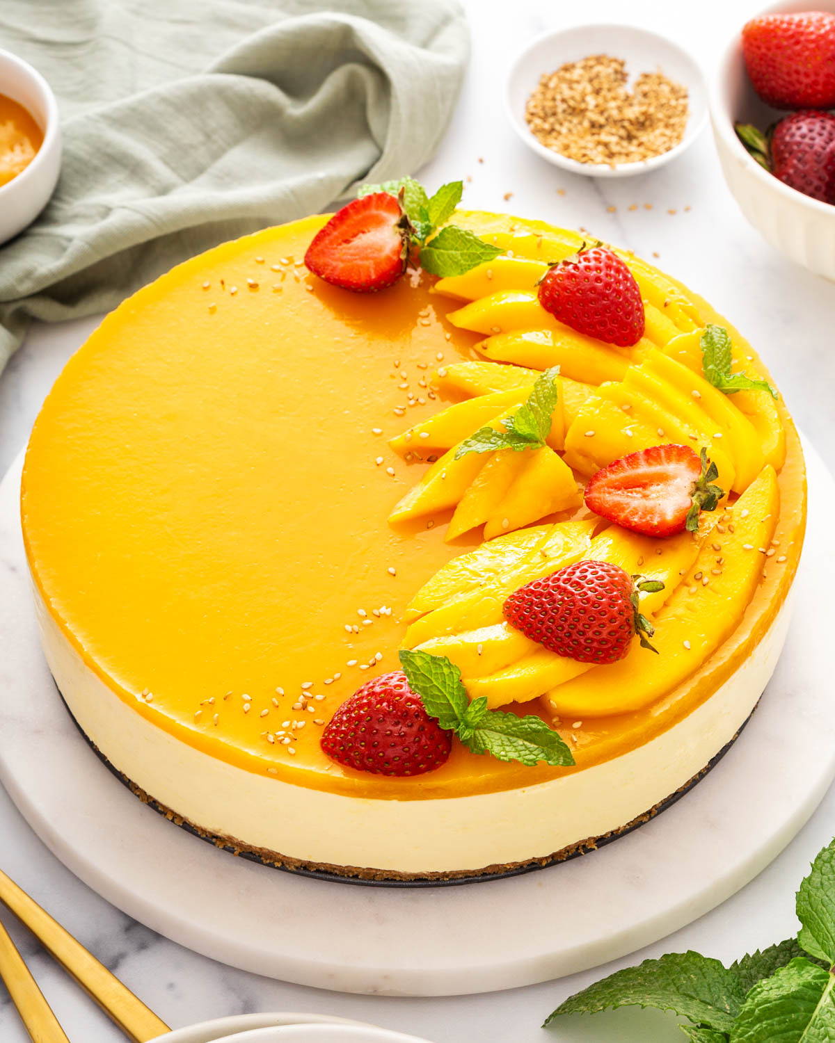 A ¾ view of a mango cheesecake with mangos and strawberries on top