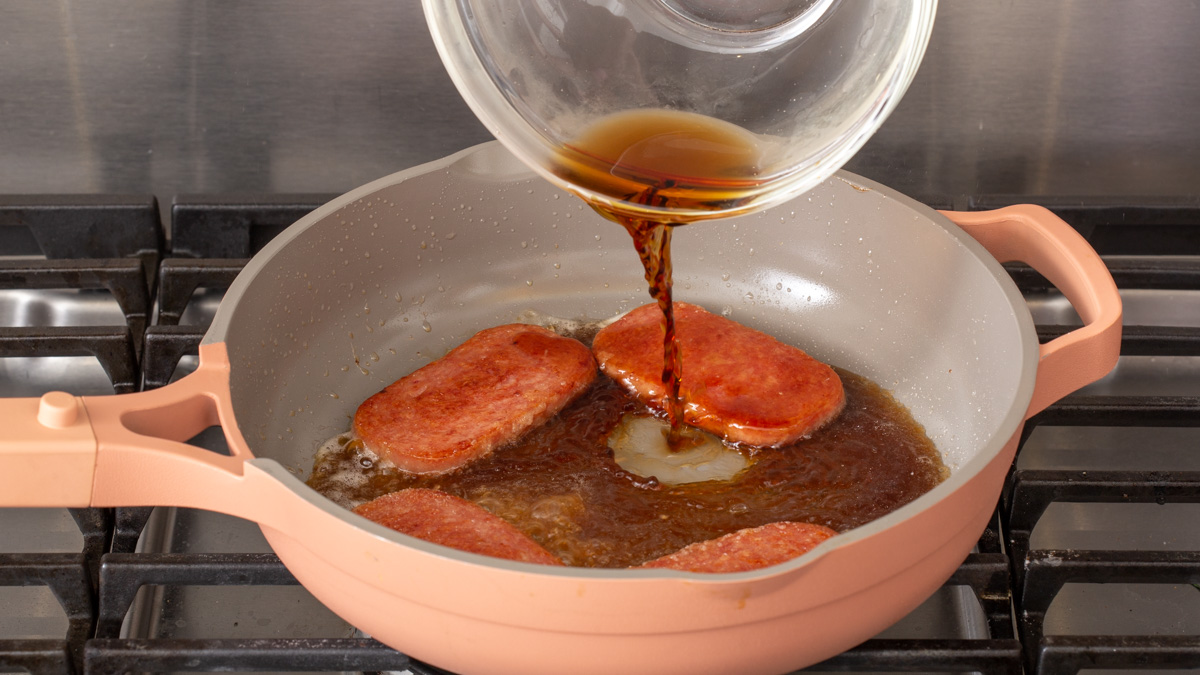 Pouring soy sauce glaze into a pan of spam cooking