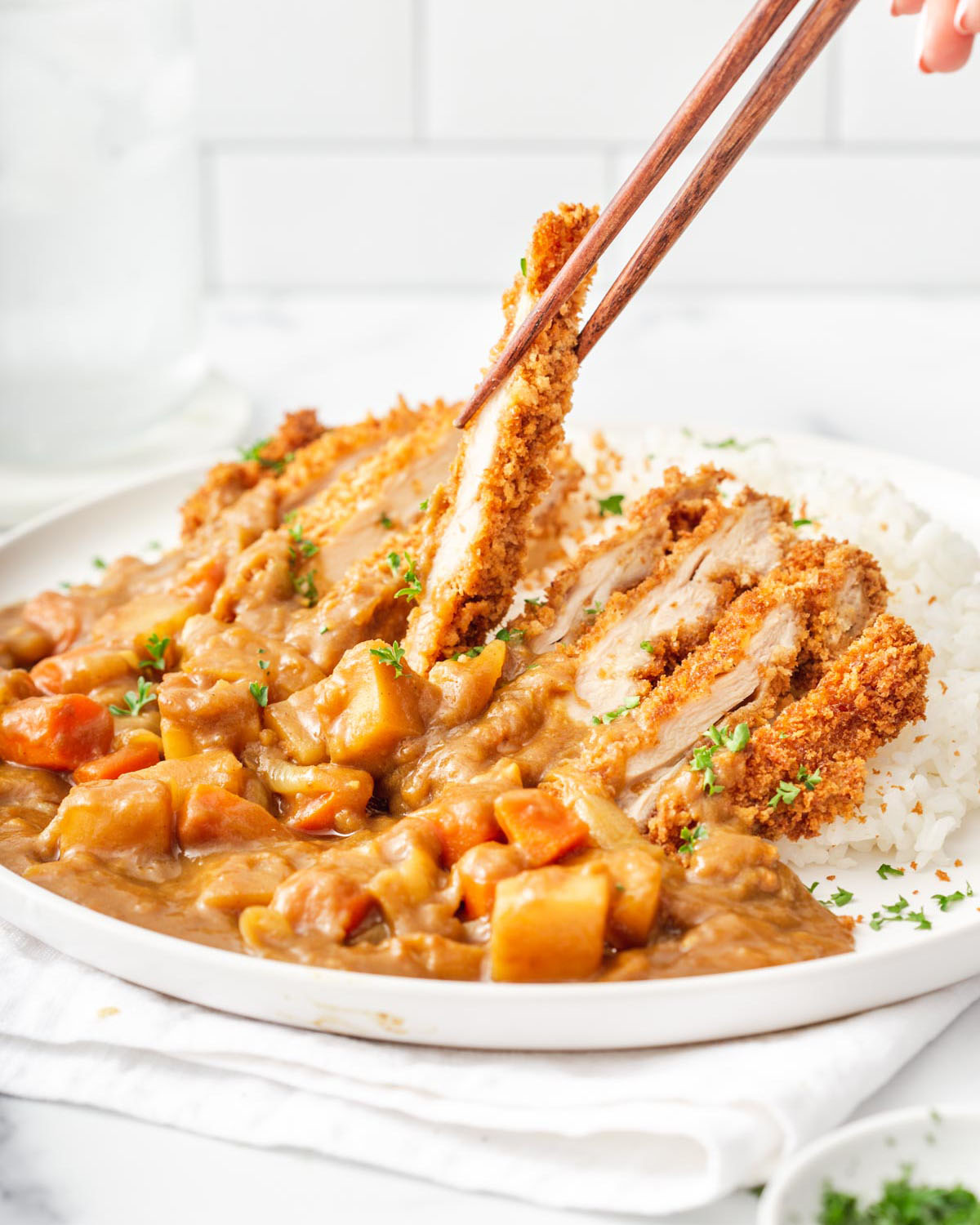 Someone lifting up a slice of fried katsu curry from a plate