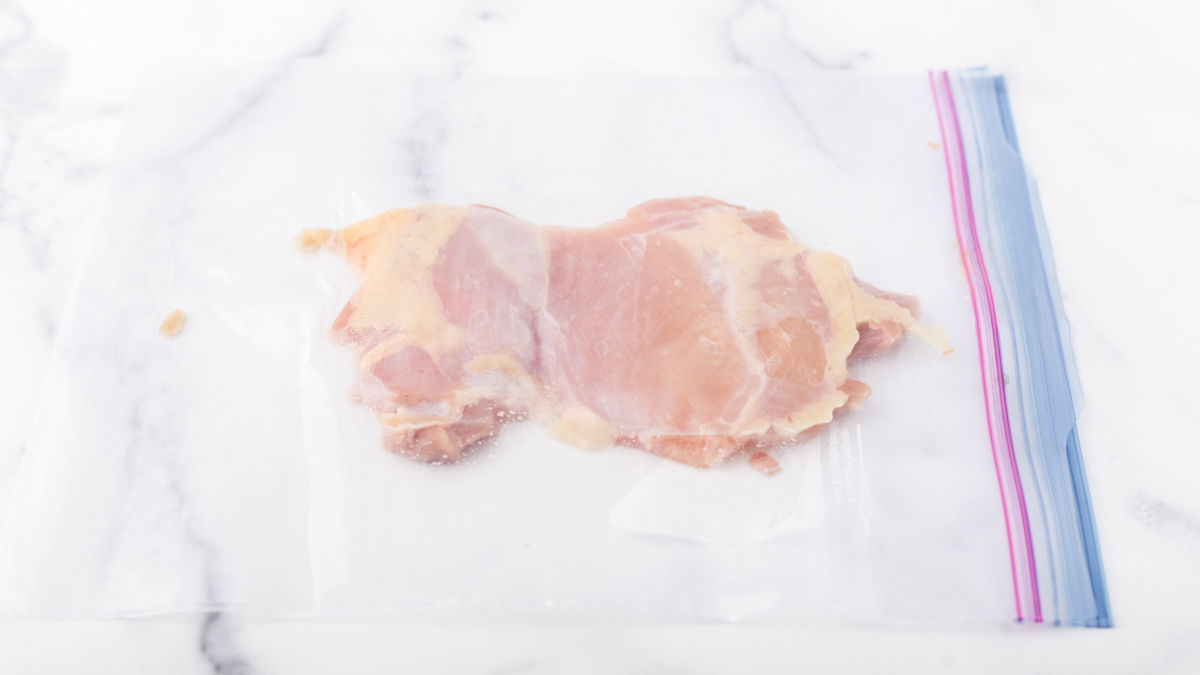 A chicken thigh covered in a ziploc bag tenderized down