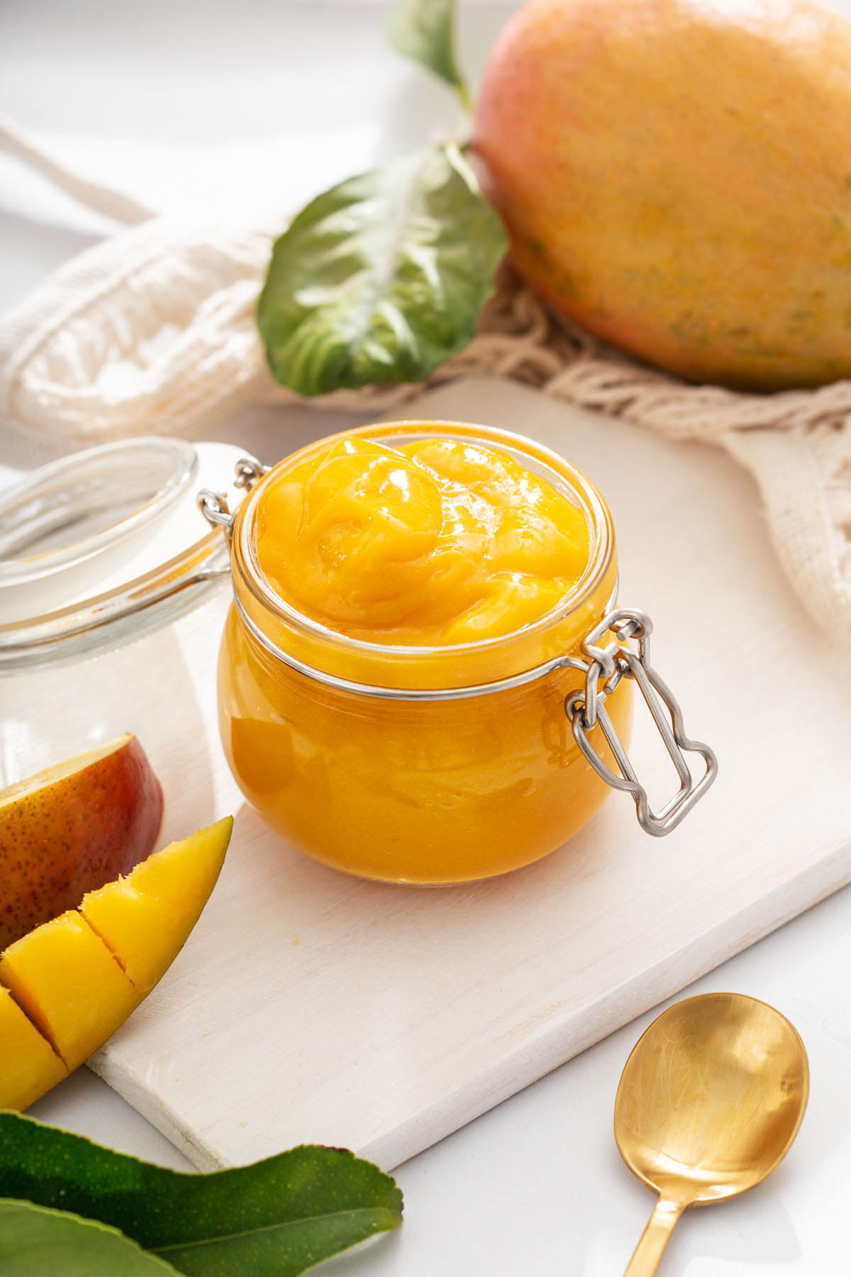 A jar of mango coulis on a table surrounded by fresh mango