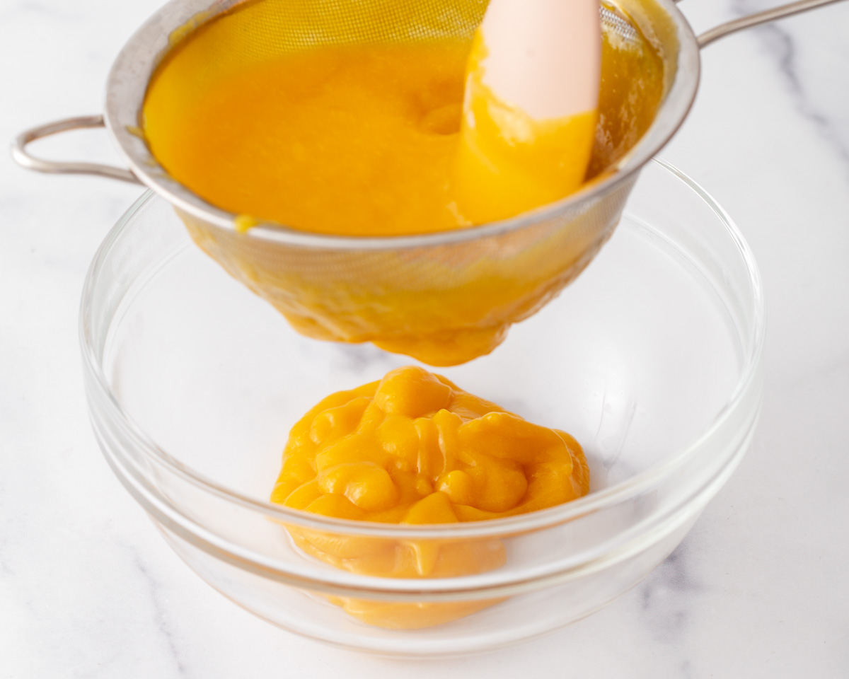 Someone straining mango puree into a bowl