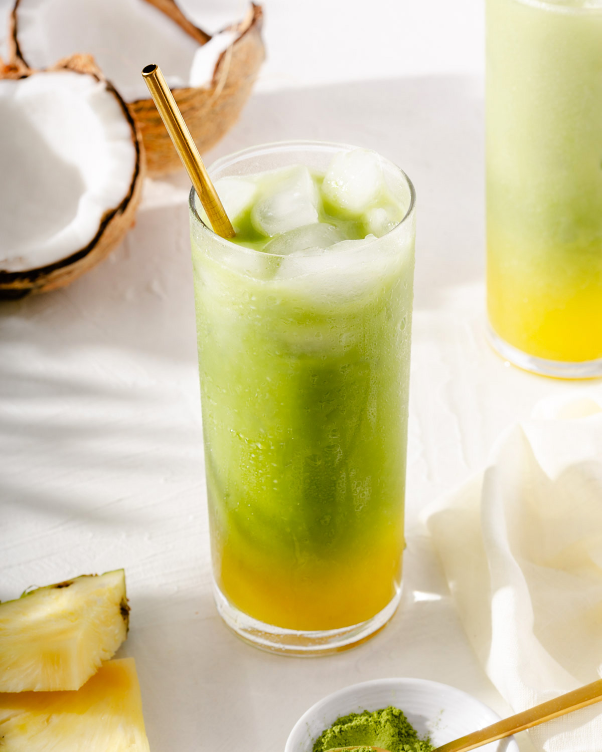 A cold glass of matcha and fresh pineapple juice with fresh pineapple and coconut nearby