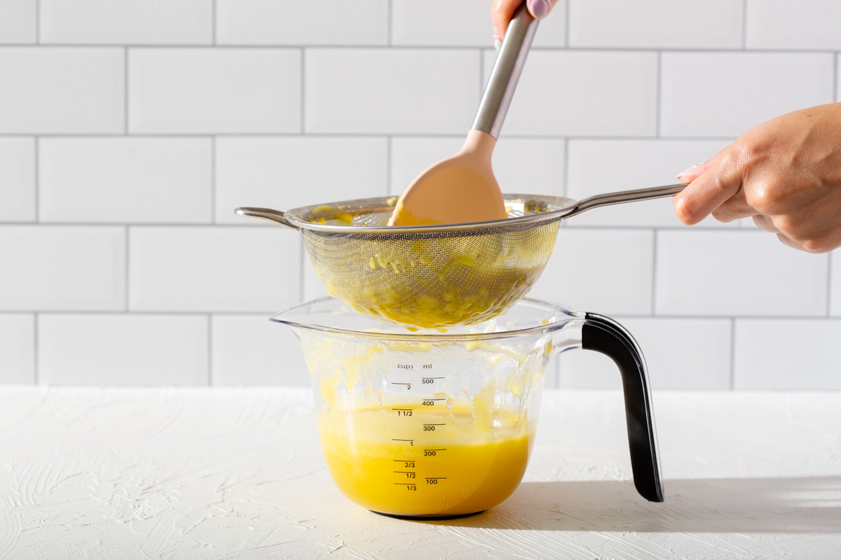 Straining pureed pineapple through a mesh sifter into a measuring cup