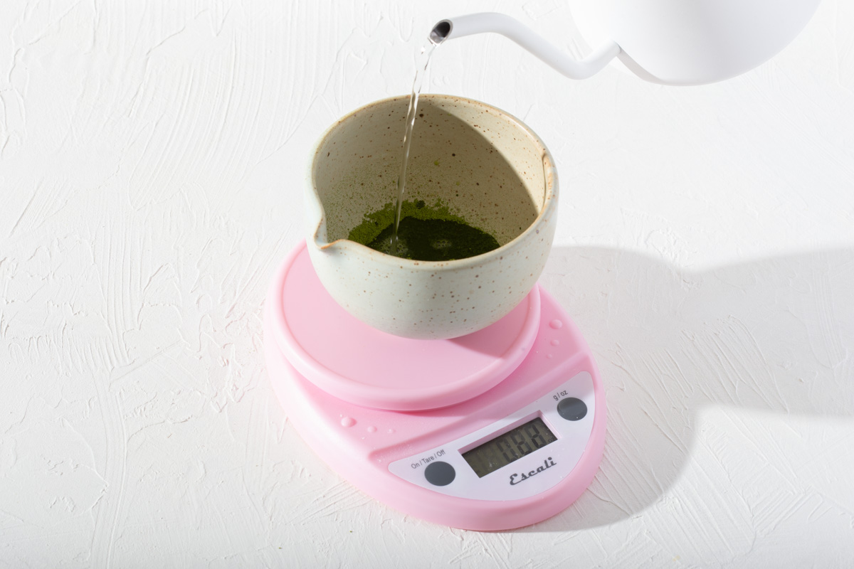 Someone measuring the precise amount of hot water into a matcha bowl with matcha powder