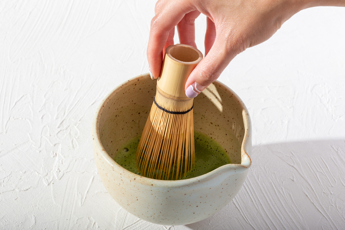 Someone whisking matcha in a bowl with a bamboo whisk