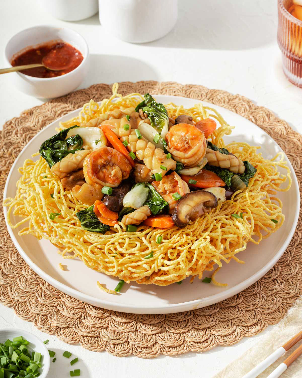 A plate with fried noodles topped with stir fry surrounded by a dinner table setting