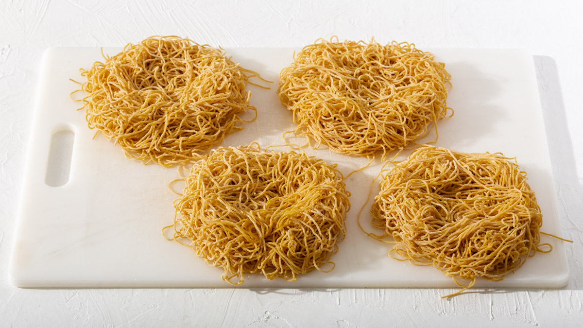 Four piles of noodles shaped into nest shapes sitting on a cutting board