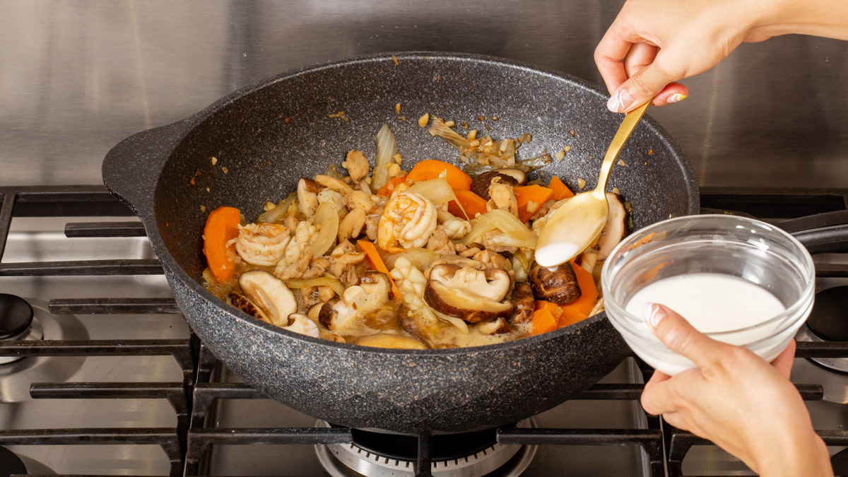 Someone adding corn starch slurry into a wok full of proteins and vegetables