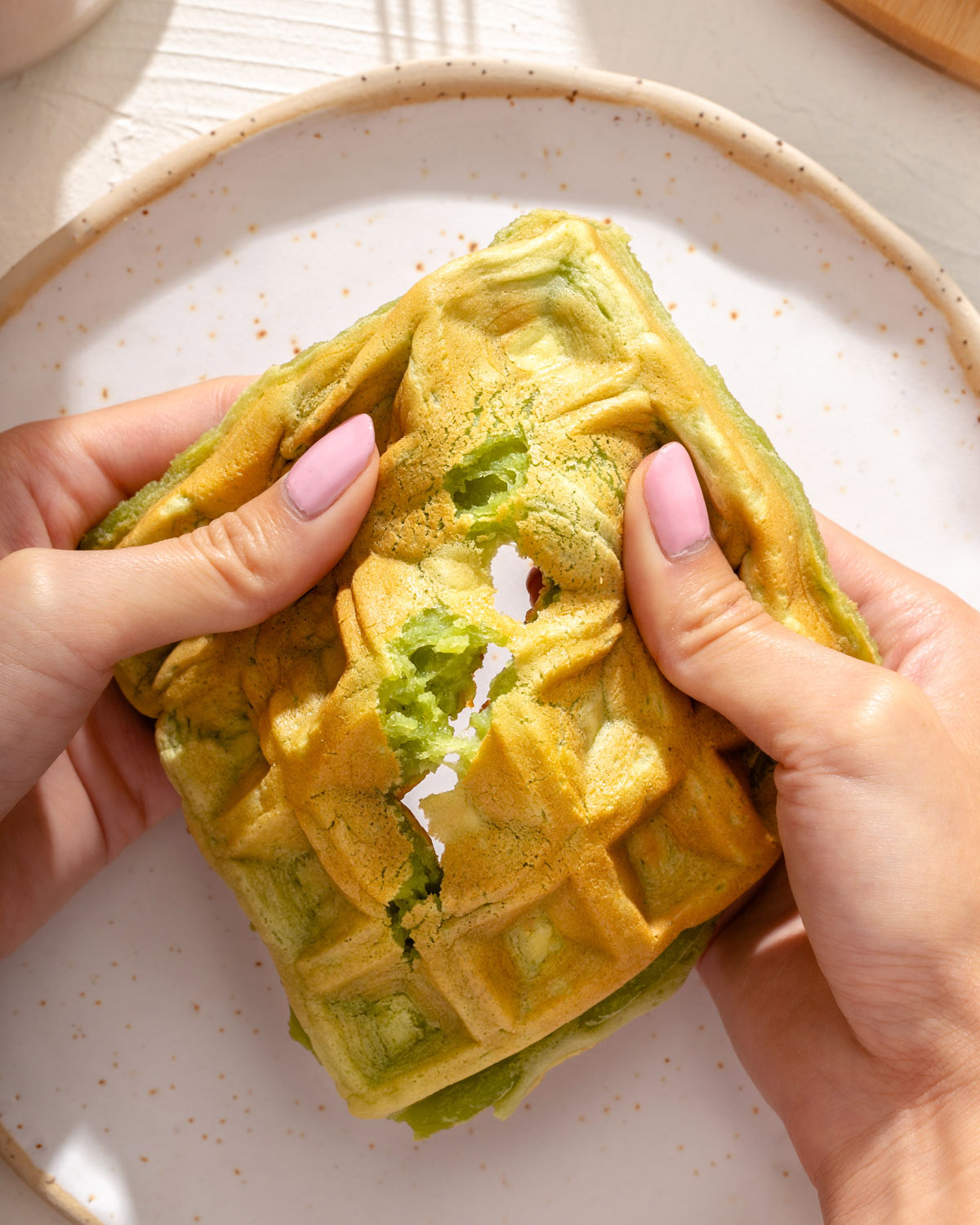 Someone pulling apart a pandan waffle to show the inside texture