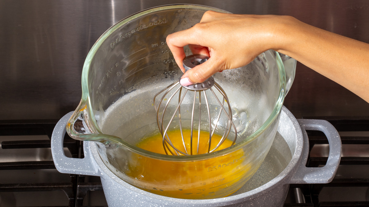 Someone whisking egg inside a bowl over a double boiler on the stove