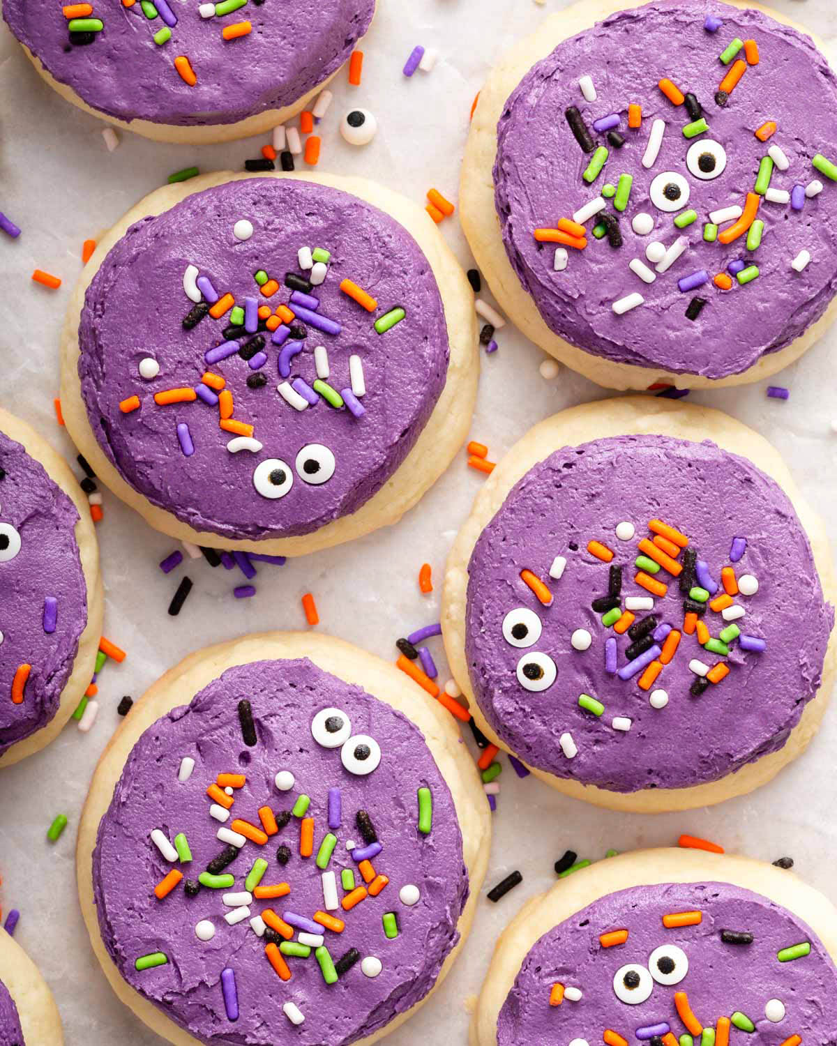 Cookies lying on parchment paper with icing, sprinkles, and eyes