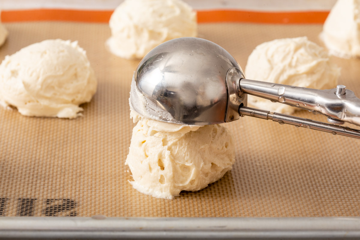 Someone scooping cookie batter onto a tray with a slipmat