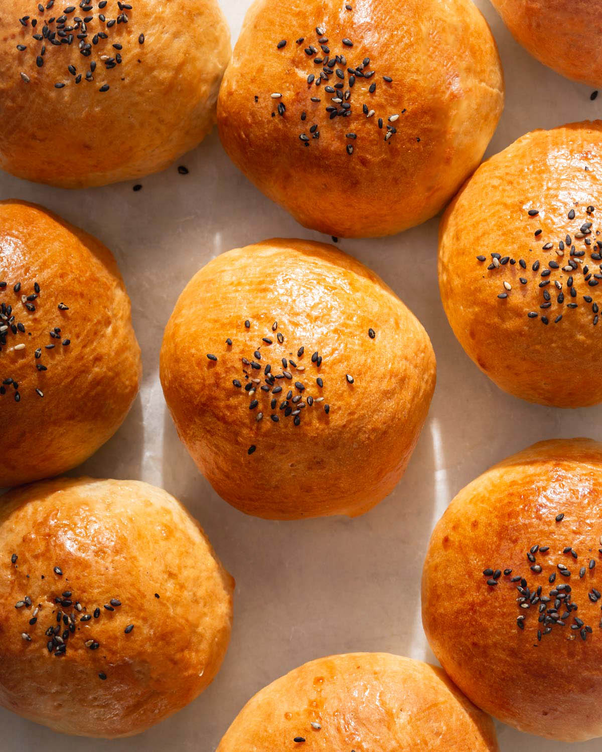 Looking down onto a tray of baked buns topped with sesame seeds.