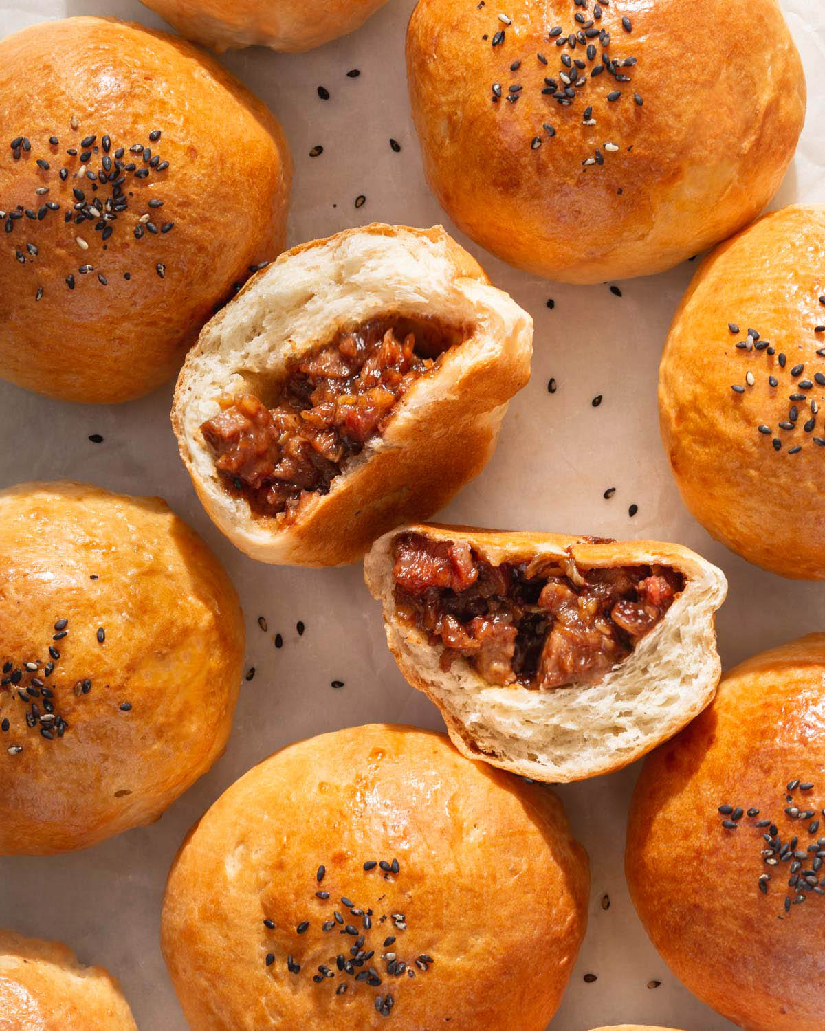 Looking down onto a tray of baked pork buns with a bun split open showing the stuffing.
