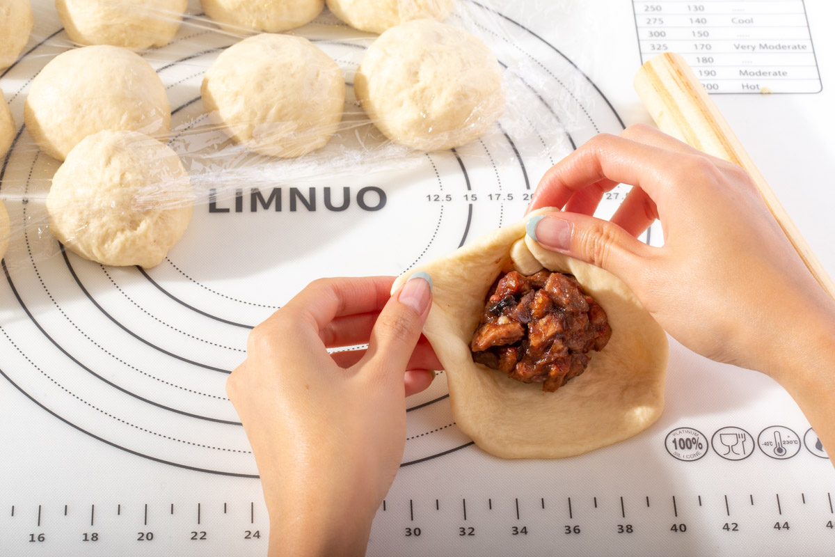 Stuffing a ball of char siu pork inside dough to make a stuffed bun.