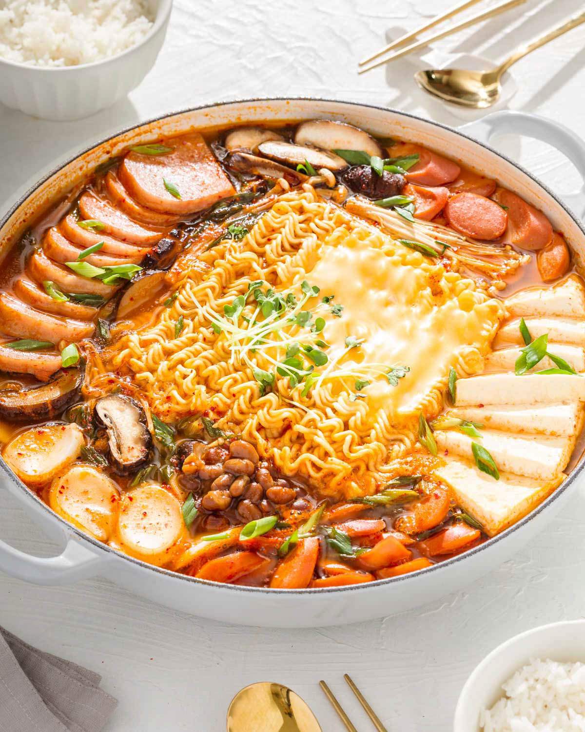 A large pot of Korean army stew surrounded by a table spread.