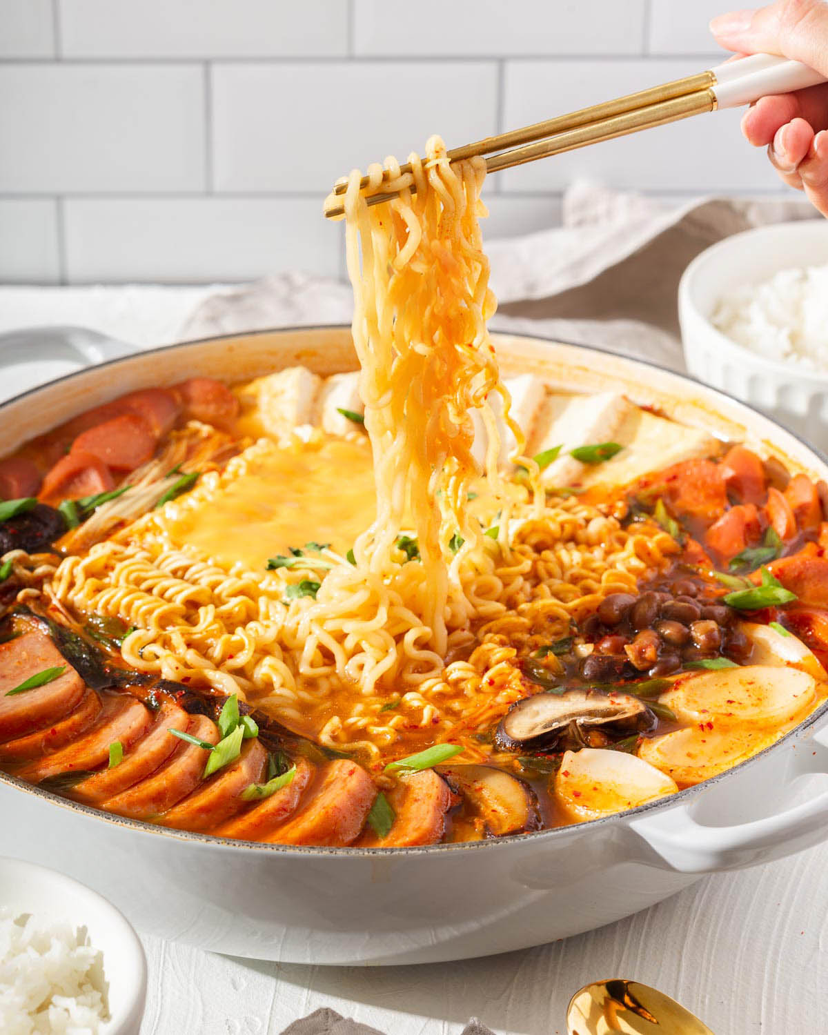 Lifting up instant ramen noodles from a large pot of army stew.