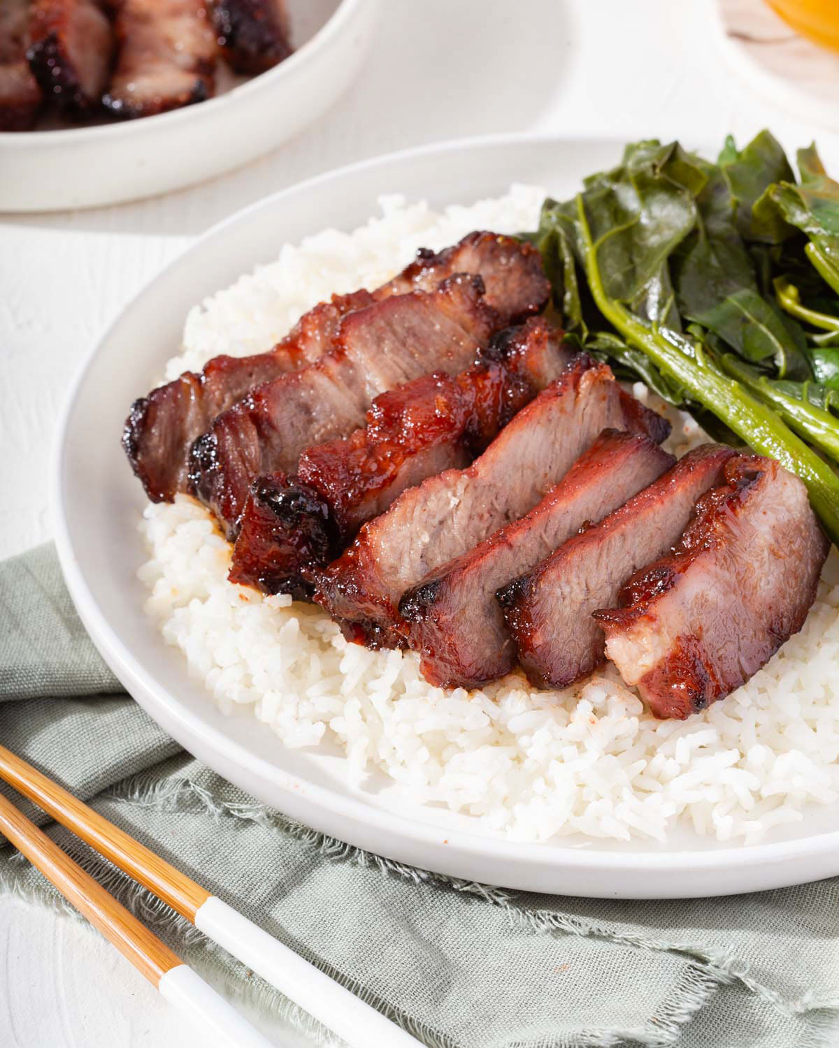 A plate of Chinese bbq pork sitting on rice with greens on the side.