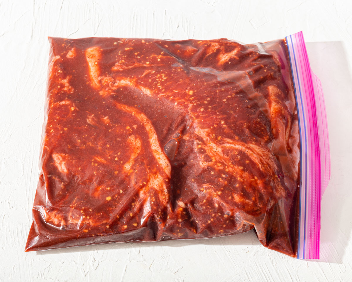 Marinading pork cuts in a large ziploc bag with a red BBQ marinade.