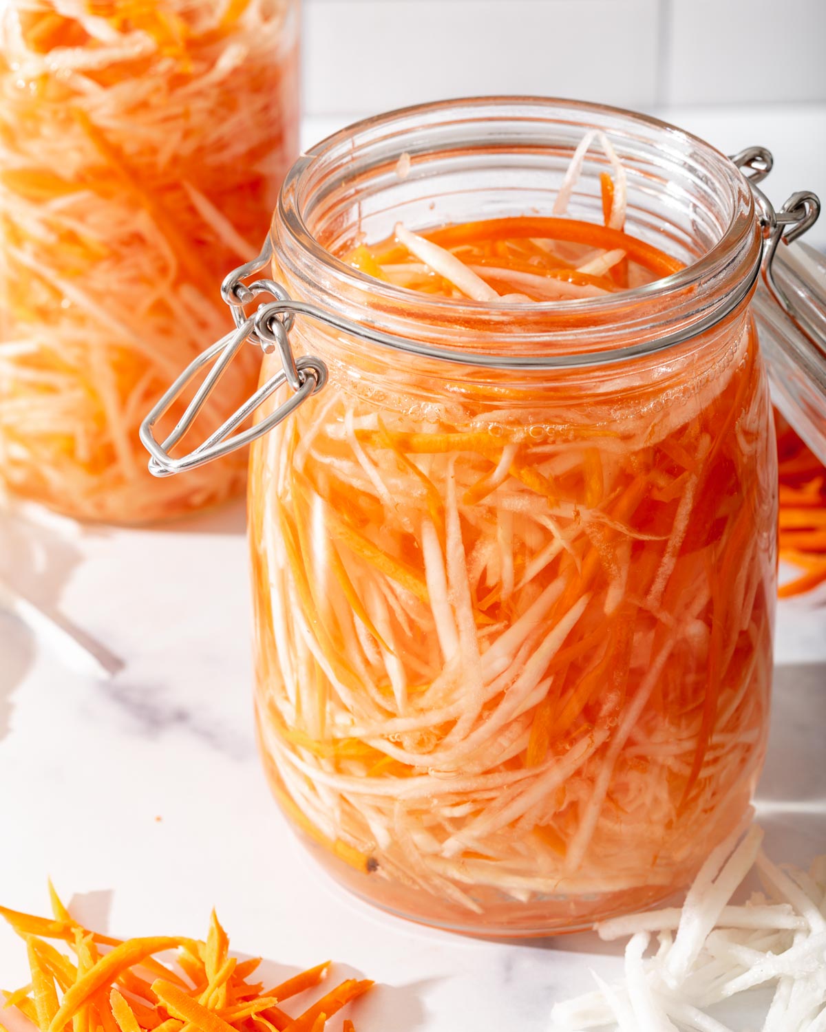 An open jar of carrots and daikon on a counter with another jar nearby.