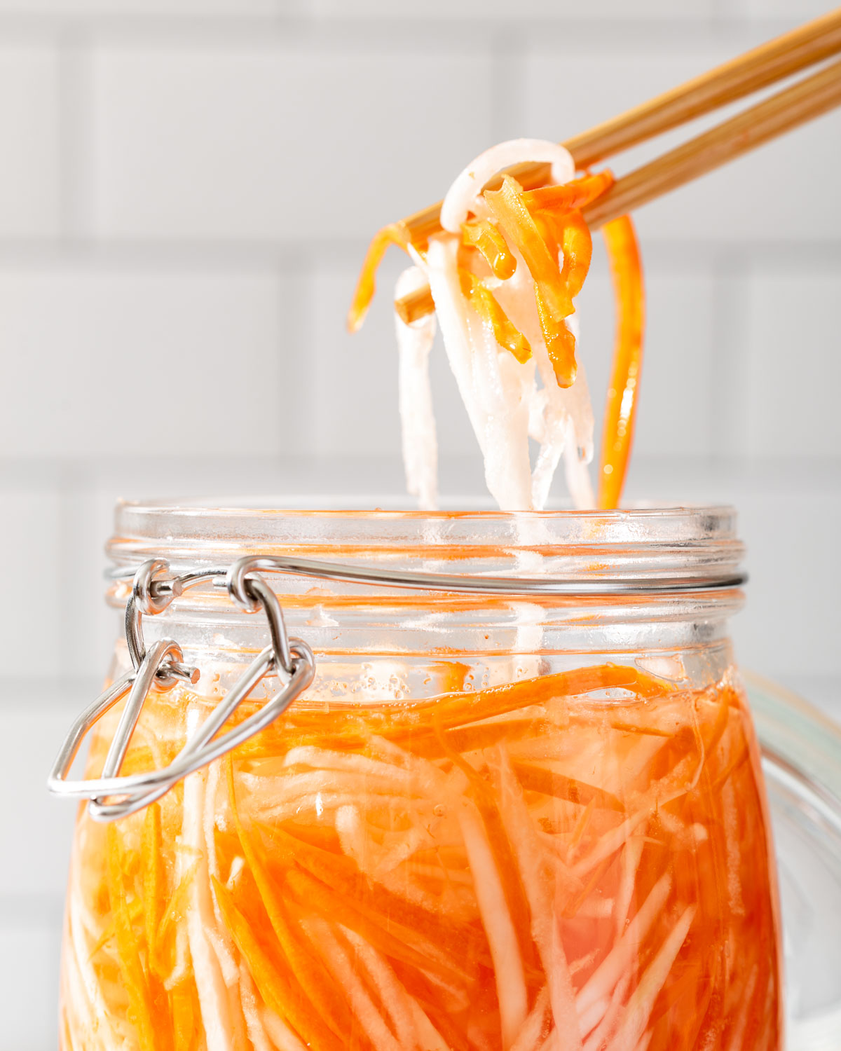 Chopsticks lifting up pickled do chua from a jar